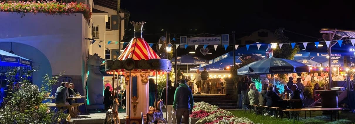 Abendliche Wiesn im Biergarten des Ratskellers Schliersee mit kleinem Kinderkarussell vor dem Rathaus.